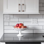 Shows dishwasher with gold handle, black cabinets, and white subway tile backsplash. The backsplash has black grout