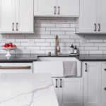 Shows the white farmhouse sink with white tile background.