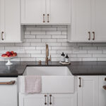 Shows white farmhouse sink, with the dishwasher and oven's gold handles.