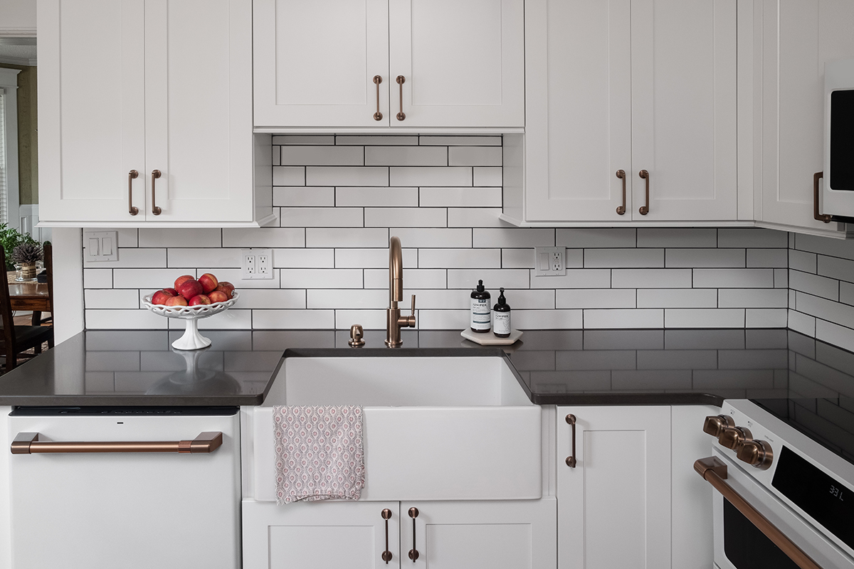 Shows white farmhouse sink, with the dishwasher and oven's gold handles.