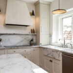 white kitchen cabinets with white marbled stone countertops. Large white range hood, and stainless steel dishwasher.