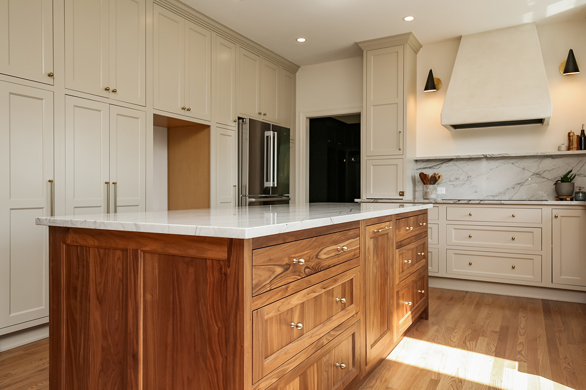 white cream kitchen. The outer lining cabinets are all white, the island cabinetry is marbled brown wood. There are marbled white stone countertops as well.