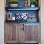 Shows the built in shelving and cabinets around the tv. There are two shelves above a cabinet that matches the cabinets of the wet bar.