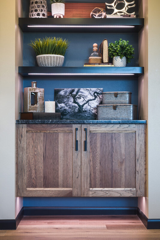 Shows the built in shelving and cabinets around the tv. There are two shelves above a cabinet that matches the cabinets of the wet bar.