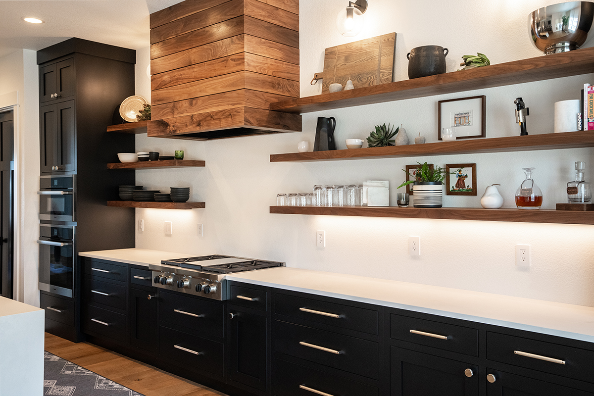 Black cabinets on the lower half of the kitchen with walnut shelves. White counters are shown with a featured a walnut hood.