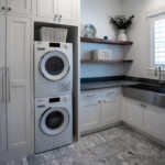 White built in cabinets around the washer and dryer. A sink in the laundry room surrounded by dark grey cabinets.