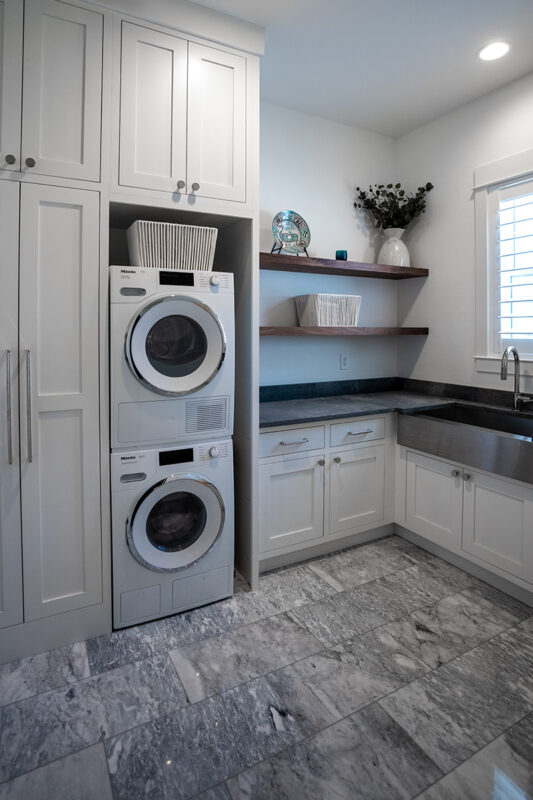 White built in cabinets around the washer and dryer. A sink in the laundry room surrounded by dark grey cabinets.
