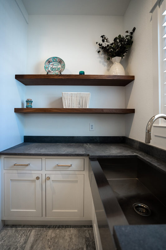 Built in walnut shelves over white cabinets and black counters in the laundry room