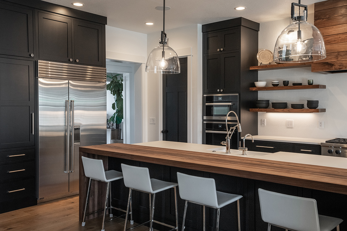 Black, white, and walnut kitchen features are show here. The bar top of the island is made of walnut with modern white chairs below.