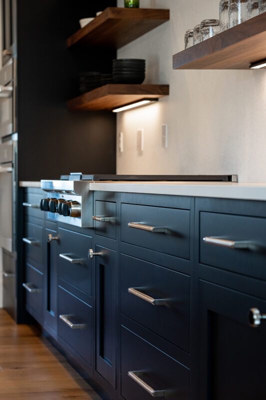 Shows the black cabinets with silver handles and the built in lights under the walnut shelving.