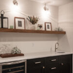 The wine fridge under a white counter next to black cabinets with a hand washing sink.