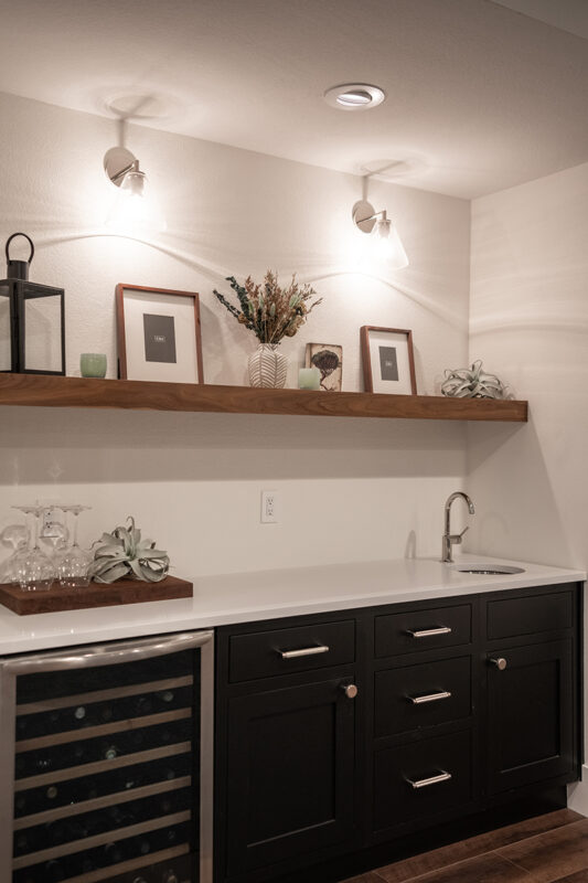 The wine fridge under a white counter next to black cabinets with a hand washing sink.