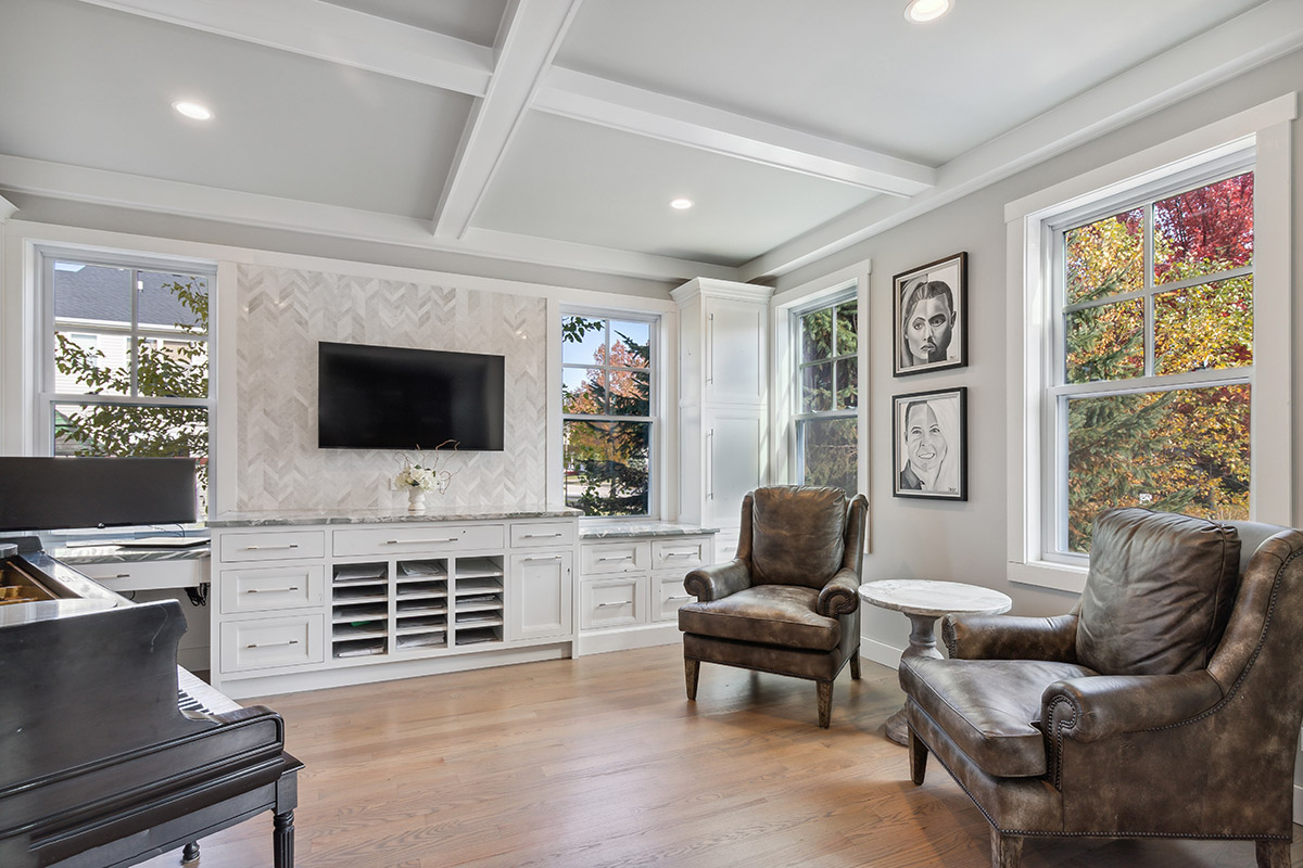 Shows a peak of the piano on the left side of the photo with sitting room on the right side of the view. There are two overstuffed chairs that line the left wall. The built in cabinets are along the back wall.