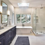 Shows the view of the double vanity with the blue cabinets, soaking tub, and glass shower.