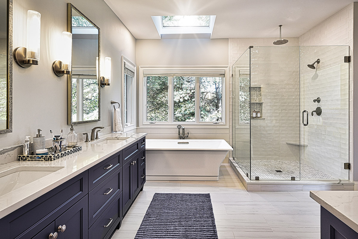 Shows the view of the double vanity with the blue cabinets, soaking tub, and glass shower.