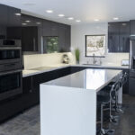 Shiny dark grey cabinets line the walls. The island and the countertop are glossy white.