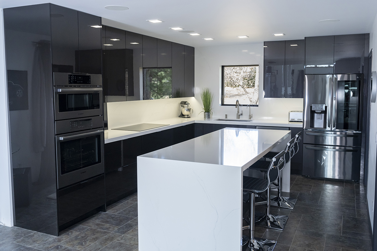 Shiny dark grey cabinets line the walls. The island and the countertop are glossy white.