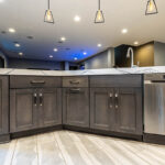 Another view of the grey cabinets under the sink with the stainless steel hardware next to dishwasher.