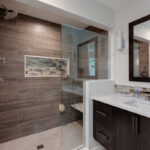 A big glass shower with multiple shower heads. The shelving is a built in box into the wall.