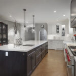 A dark brown island with white cabinets is in the middle of the room. The cabinets along the wall are white. There is a large commercial stove in the middle of the white cabinets.