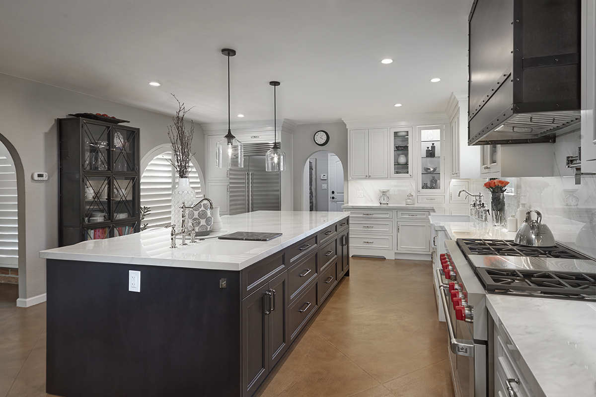 A dark brown island with white cabinets is in the middle of the room. The cabinets along the wall are white. There is a large commercial stove in the middle of the white cabinets.