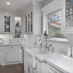 A white farmhouse kitchen sink with delicate silver sink hardware.