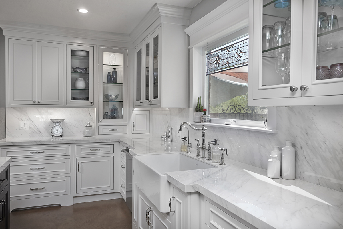 A white farmhouse kitchen sink with delicate silver sink hardware.