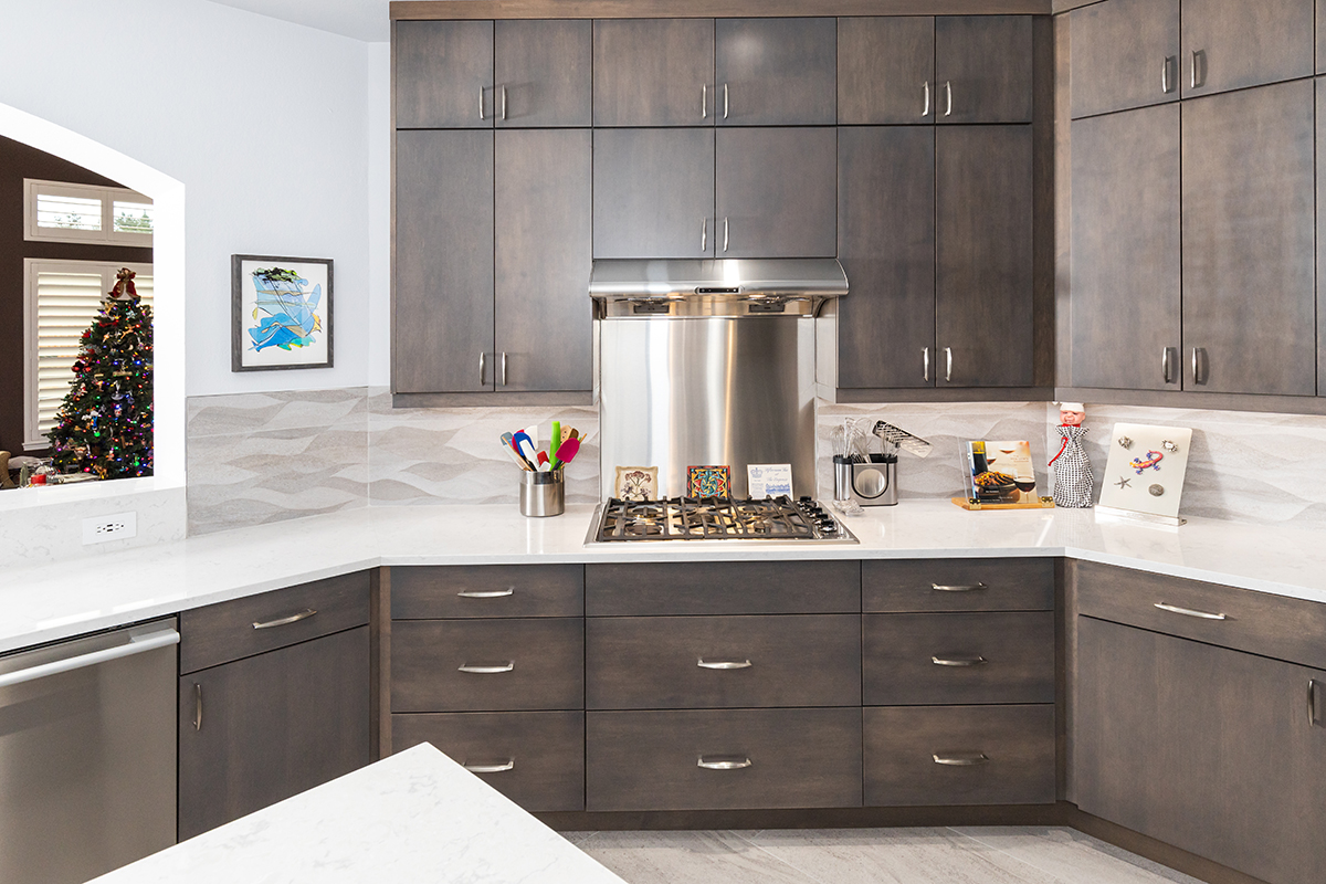 brown kitchen cabinetry with silver hardware and large silver hood range