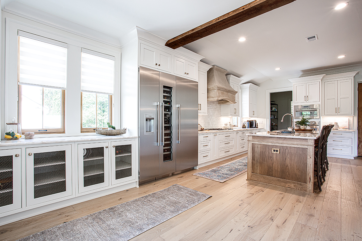 Long view of the kitchen with the big fridge, mesh-faced cabinets, and hickory island.