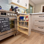 A pull out cabinet with kitchen spoons and spatulas is next to the range and oven.