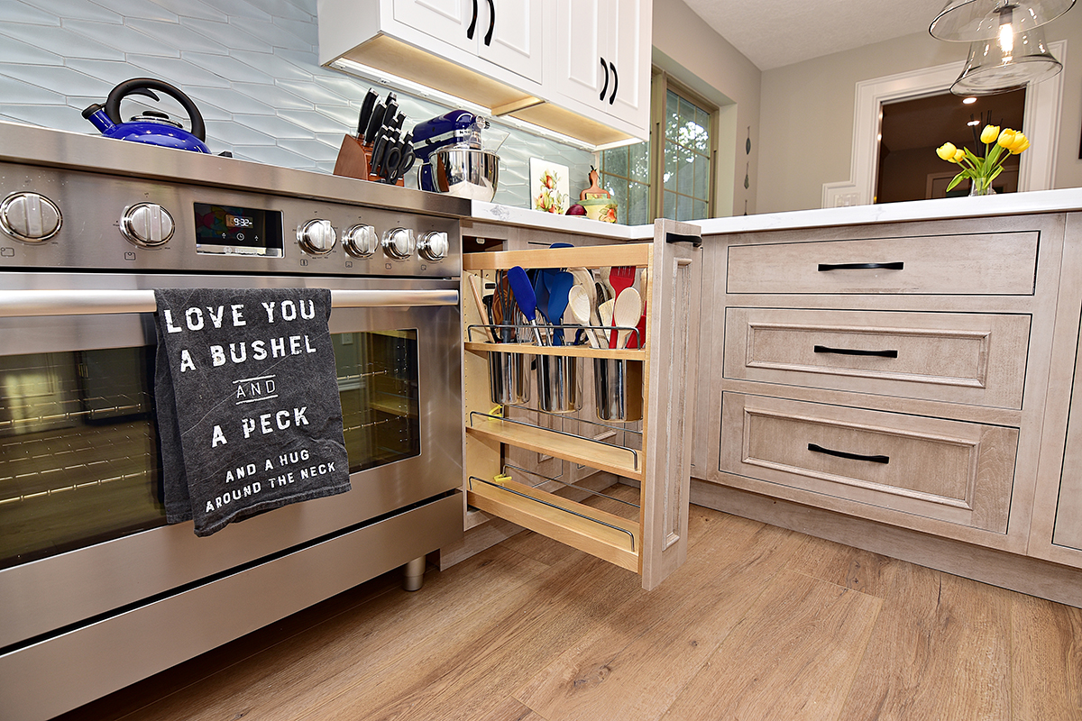 A pull out cabinet with kitchen spoons and spatulas is next to the range and oven.