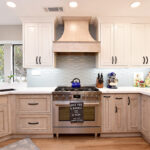 A wide view of the oven and range with the range hood. The light blue, wavy backsplash, and cabinets.