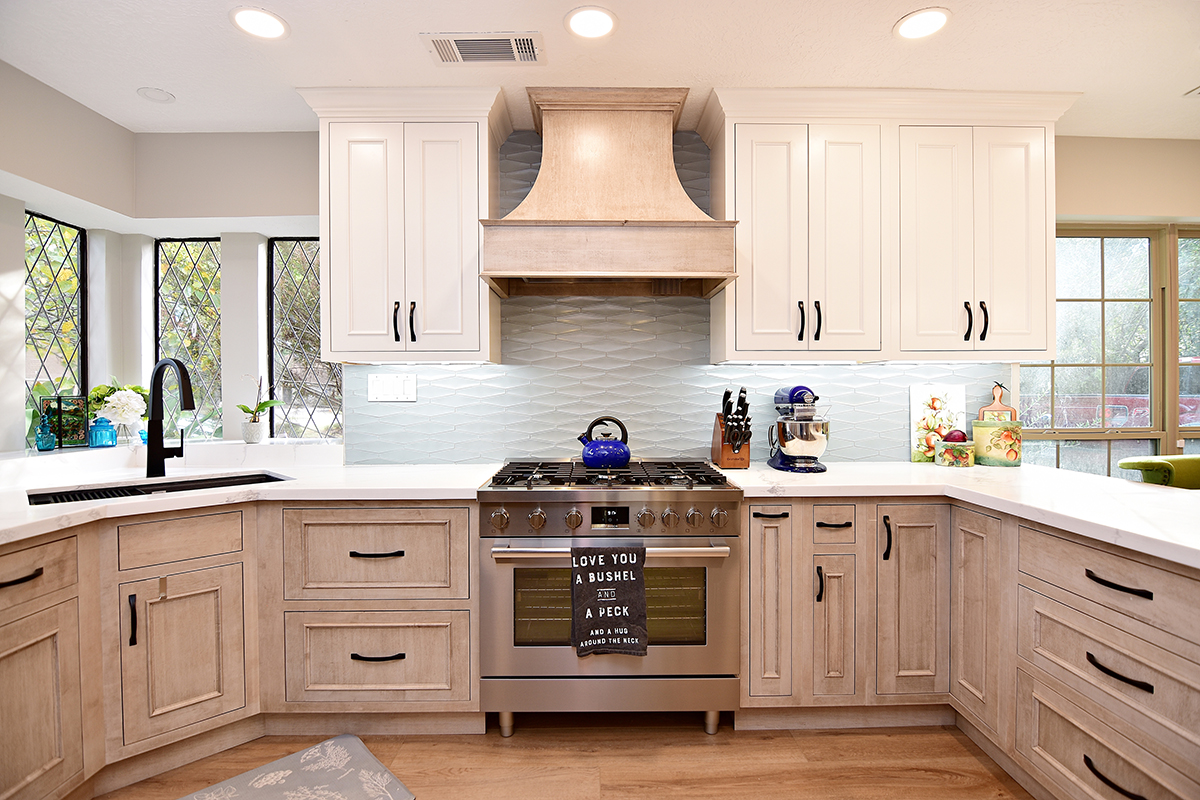 A wide view of the oven and range with the range hood. The light blue, wavy backsplash, and cabinets.