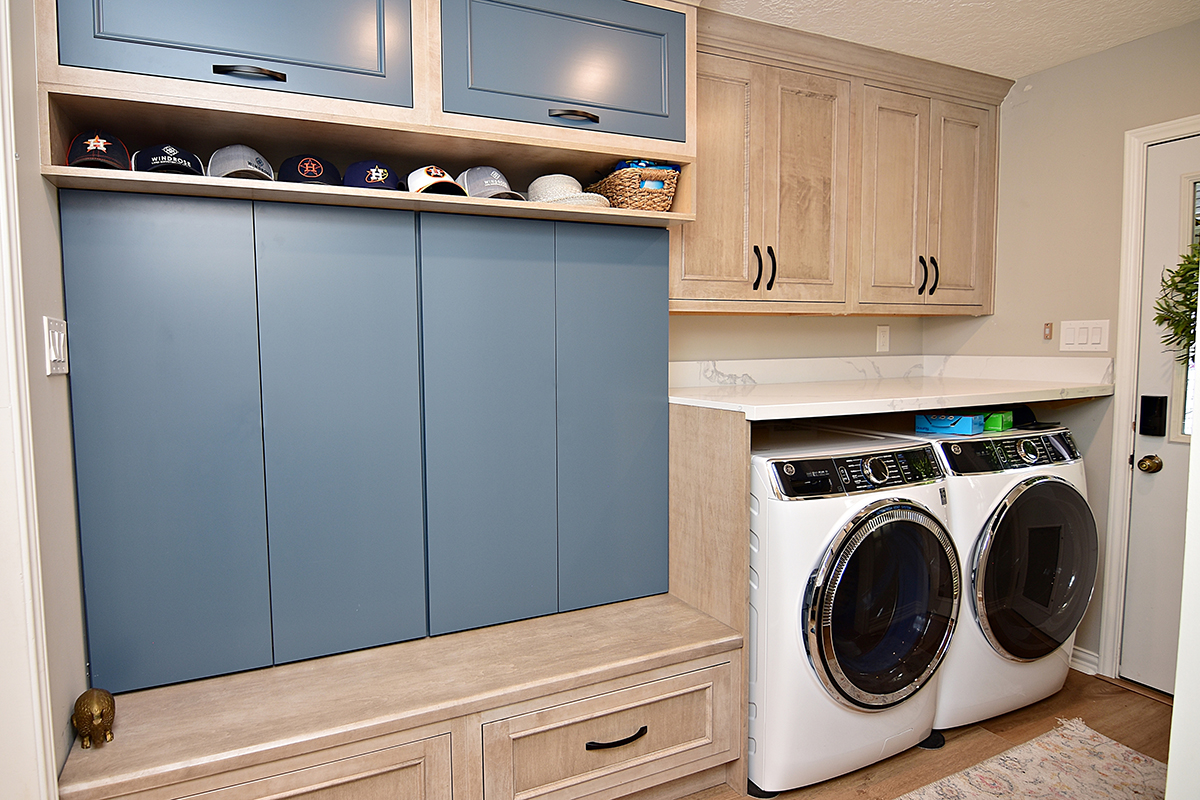 Built-in locker style storage in half of the room with the washer and dryer on the other side of the room. There are blue accents on the back wall of the locker and the upper cabinet faces.
