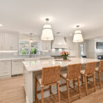 all white kitchen cabinetry with silver accents, and brown wicker chairs.