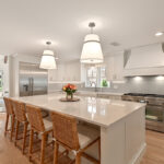 All white kitchen with wooden accent. Bright modern appliances. Brown wicker chairs.