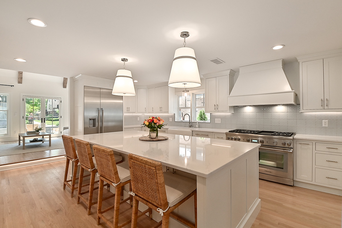 All white kitchen with wooden accent. Bright modern appliances. Brown wicker chairs.