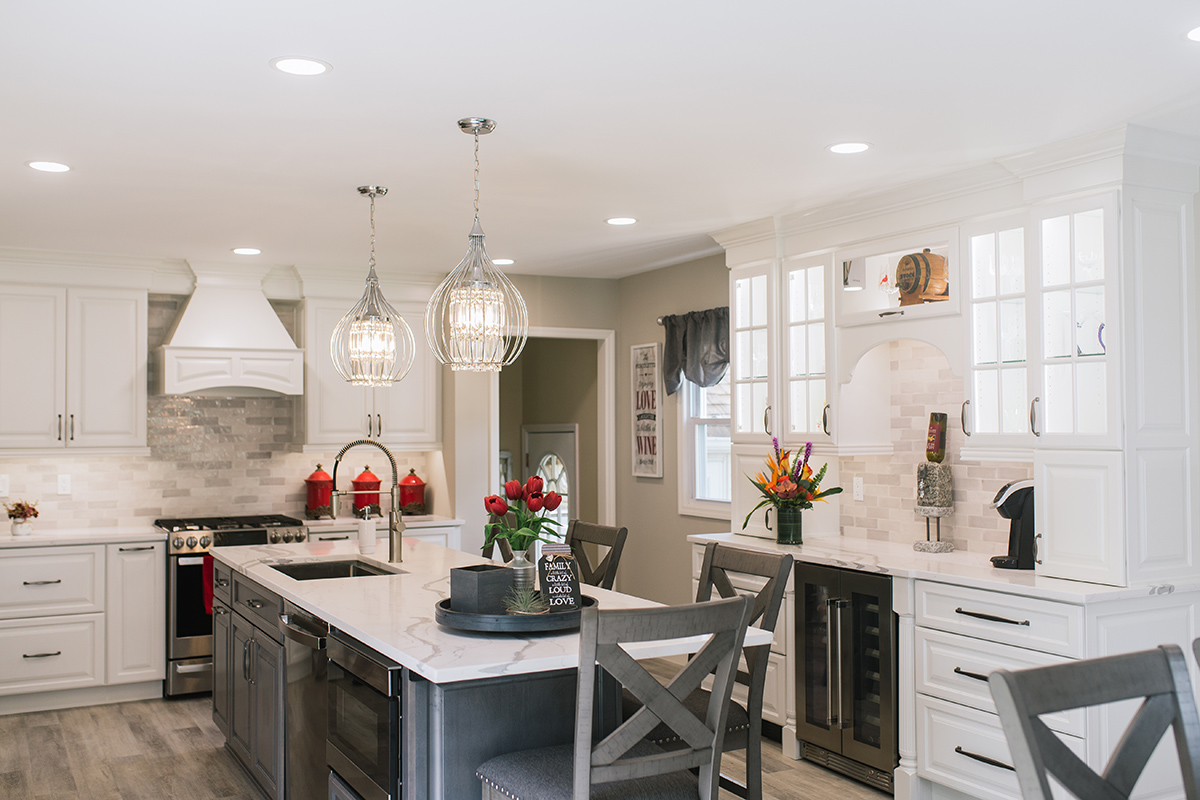 this kitchen is majority white, but the island is a dark grey color. The appliances are stainless steel, and the kitchen hard is silver. The kitchen has silver light fixtures.