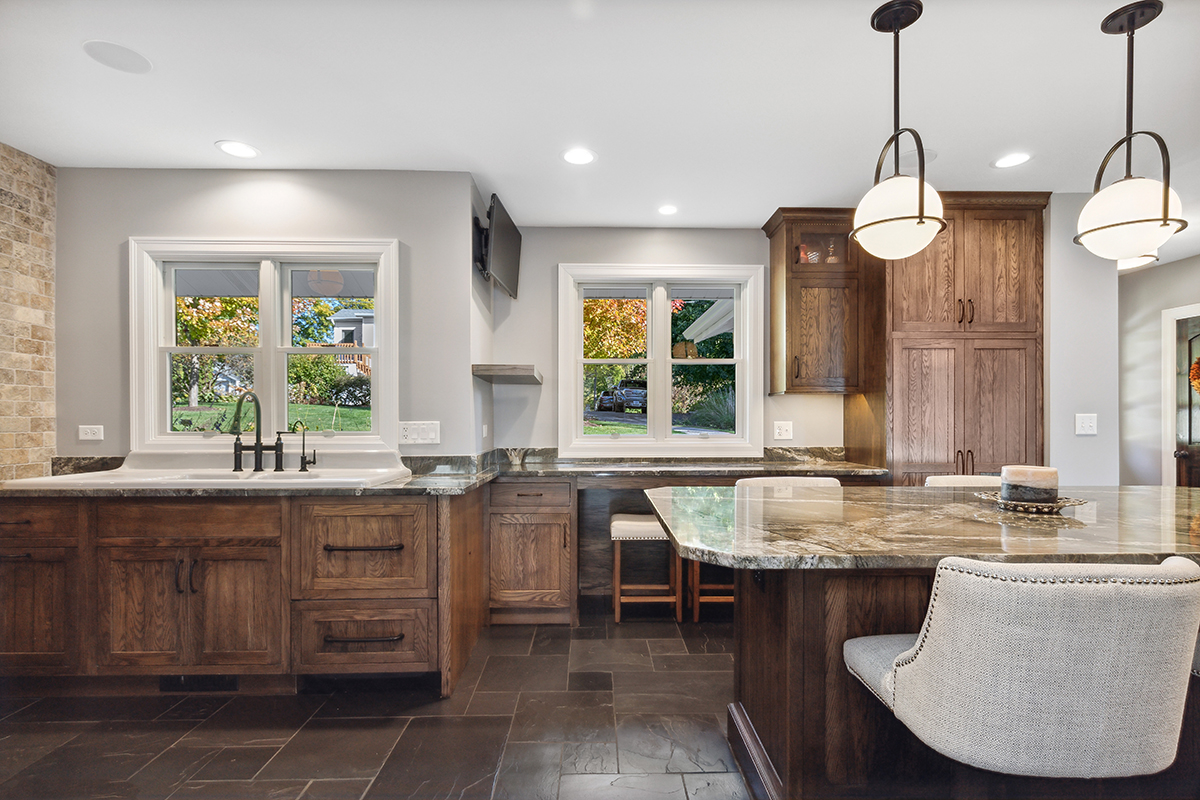 This kitchen features a large farmhouse sink with grainy wood cabinets. The counters are a brown marble.
