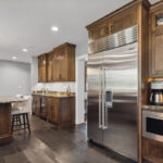large stainless steel fridge inside dark wooden cabinetry. open kitchen with stone countertop island.