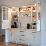 white cabinetry in coffee nook. The cabinets are lit up by internal lighting. Black handles are on the white cabinet doors.