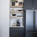 black cabinetry for coffee nook. Brown wooden shelves sit above. Brass accents on the handles and knobs.