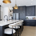 black kitchen cabinetry with white stone countertops. Brass colored accents are sprinkled throughout the kitchen.