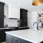 Black and white kitchen cabinetry with large white stone countertops and island. Brass finish on knobs and handles.
