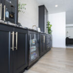 close up view of minibar with black cabinetry and silver accents. The mini fridge is stocked with beverages.