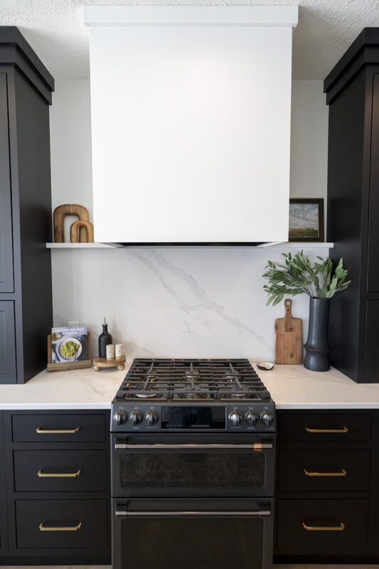 stove accompanied with black and gold cabinetry. white stone countertop and backsplash