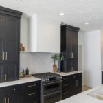 small kitchen cooking space with black inset cabinetry and bronze handles.