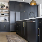 all black kitchen cabinetry with brass accents. Gray fridge and dishwasher combo