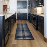 The view between the external wall and the island in the kitchen that shows the black cabinets in contrast to the white countertop and the natural wood floor.