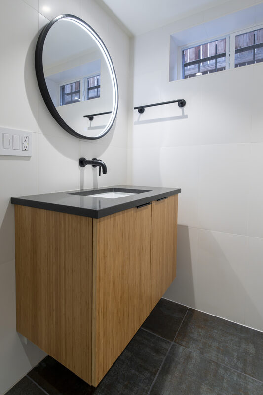 floating wood bathroom sink with gray countertop and large circular LED mirror.